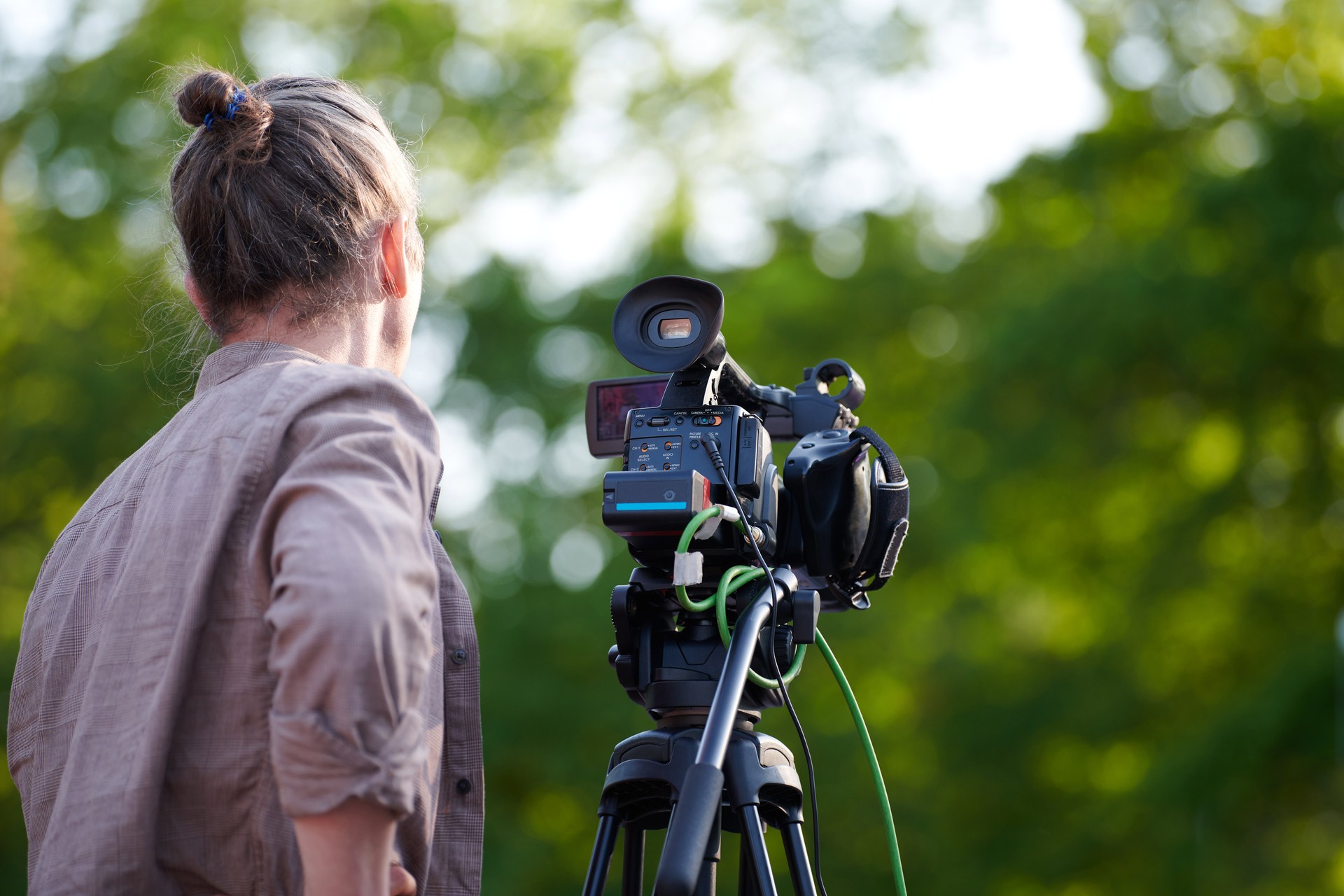 Rear view to man videographer recording outdoor movie about nature on professional camera, TV crew